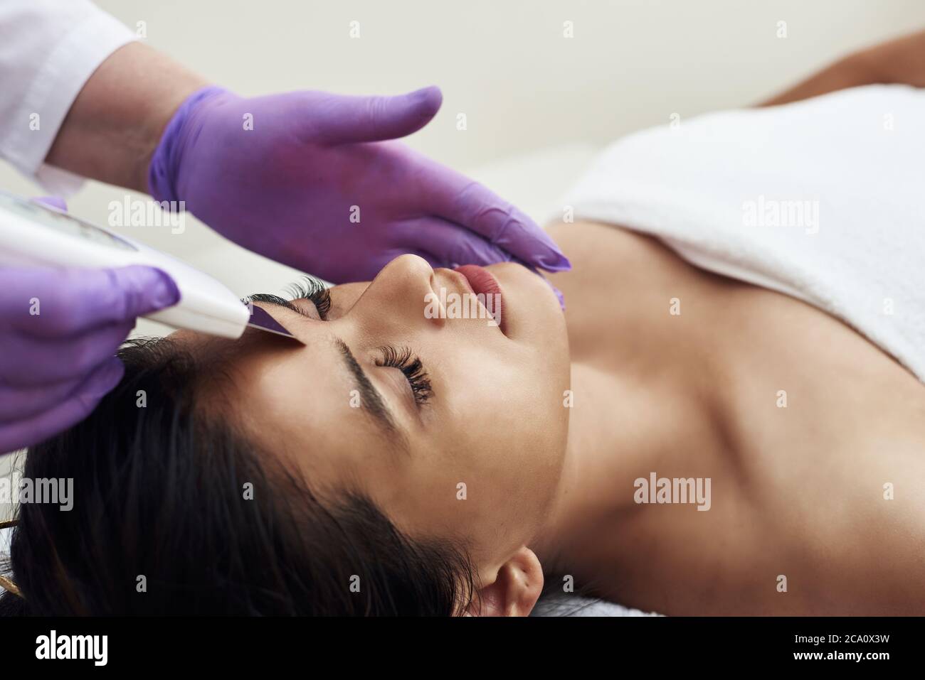 Une femme effectue un nettoyage ultrasonique du visage et de la peau à un client. Équipement moderne. Jeune jolie femme recevant des soins dans les salons de beauté et allongé sur le canapé. Banque D'Images