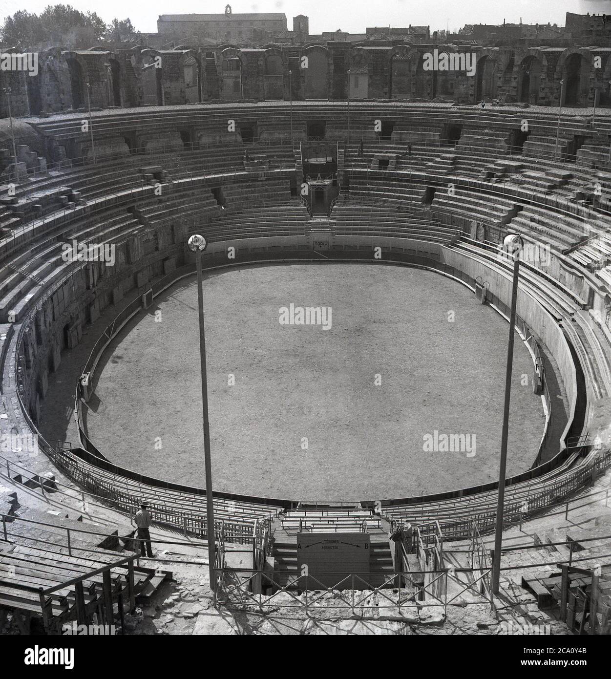 1960, vue historique de cette époque de l'ancien amphithéâtre romain d'Arles, au sud de la France, en regardant à travers et vers le bas l'arène ovale. Construit autour de 90 AD pour fournir des divertissements sous la forme de courses de Chariot et des batailles main à main de gladiateurs, il est devenu plus tard un abri pour la corde et une forteresse. Au XIXe siècle, les bâtiments à l'intérieur de l'arène ont été renversés et il est devenu, une fois de plus, un lieu de divertissement, tenant des concours de corrida et des concerts. Un amphithéâtre est dérivé du mot grec anicent meaing 'place pour l'observation'. Banque D'Images