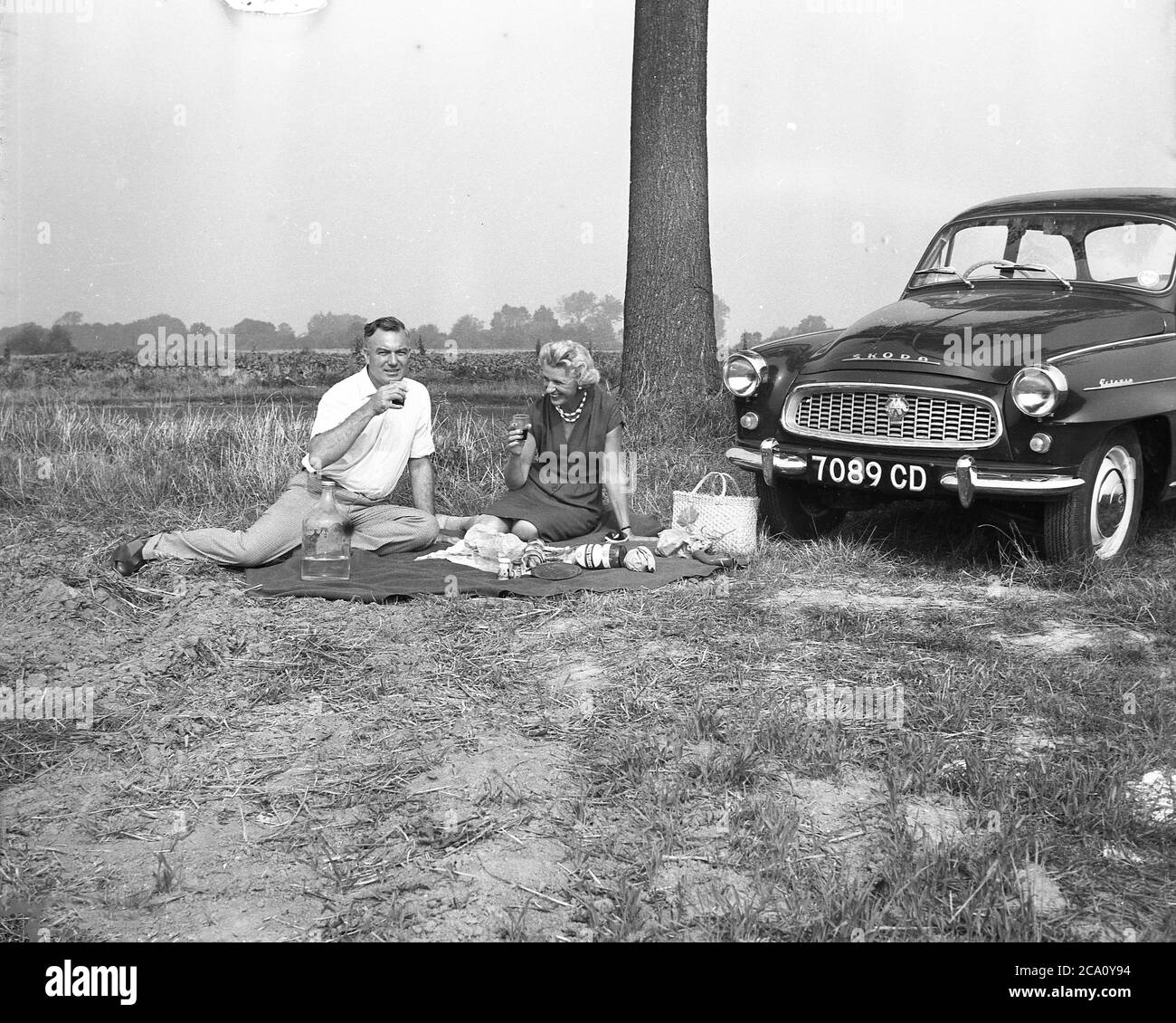 1960, historique, un couple britannique en voiture autour de la France. Assis ensemble sur une couverture avec un verre de vin rouge français et un pique-nique au bord de la route à côté de leur voiture Skoda Octavia, une petite voiture familiale de l'époque réalisée par le producteur automobile tchécoslovaque AZNP à Mlada Boleslav de 1969 à 1971. Elle a été nommée Octavia comme étant la huitième voiture produite par le constructeur automobile tchèque Skoda Auto. Banque D'Images