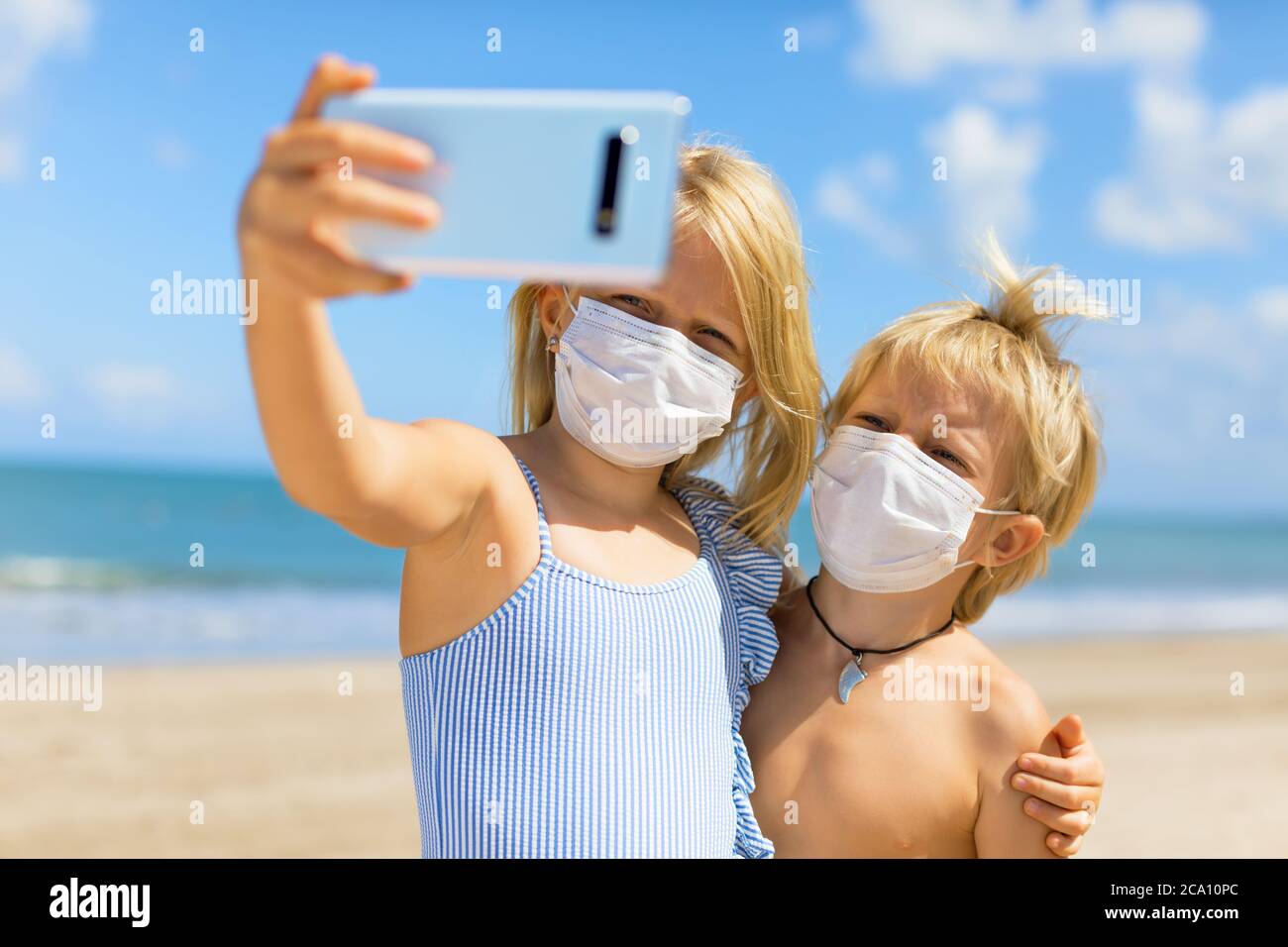 Drôle d'enfants prenant photo selfie par smartphone sur la plage tropicale de mer. Nouvelles règles pour porter un masque de couverture en tissu dans les lieux publics en raison de coronavirus COVID Banque D'Images