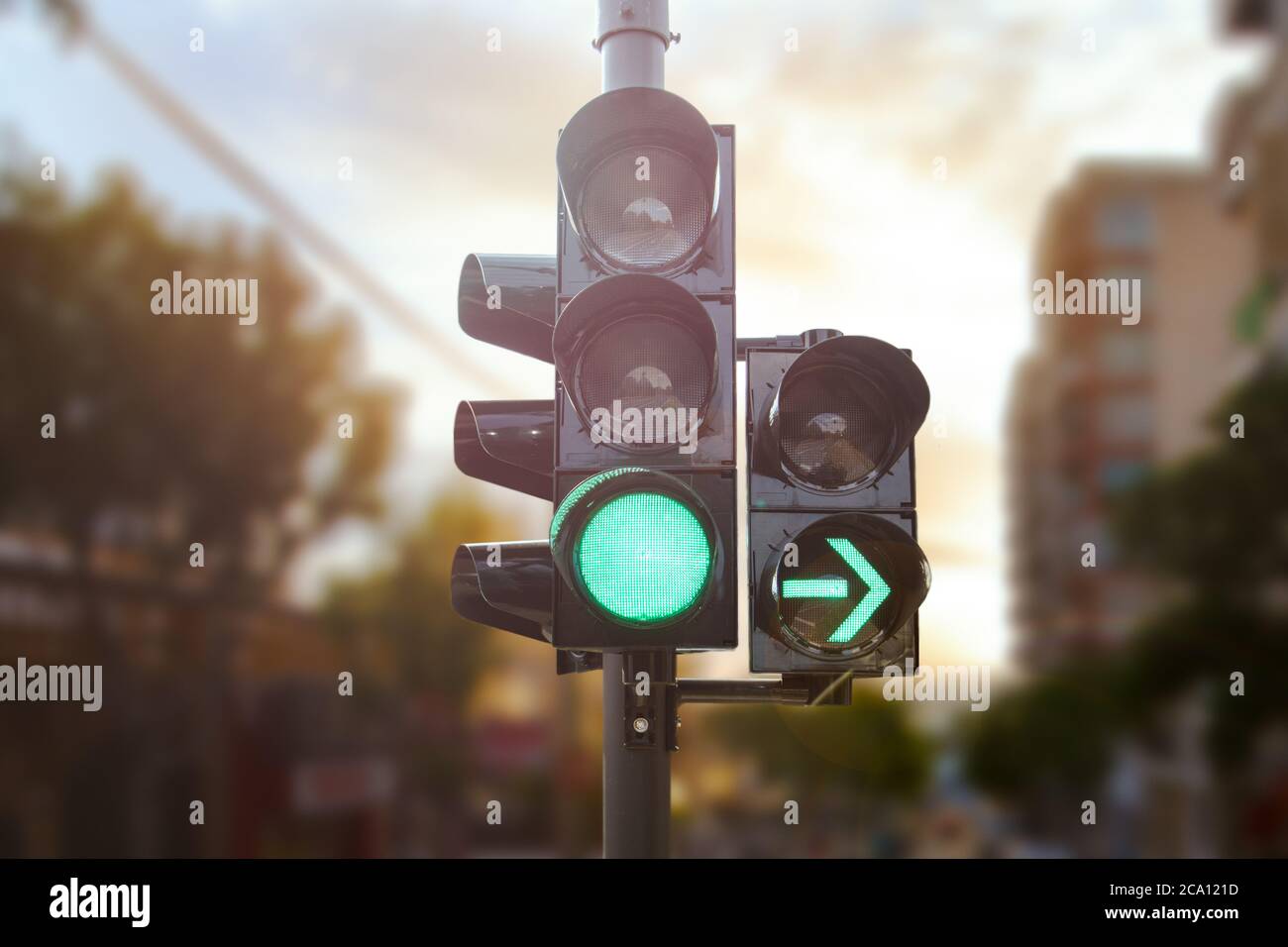 Le feu de circulation vert avec une flèche verte s'allume en ville tandis que le coucher du soleil permet à la voiture de tourner à droite Banque D'Images