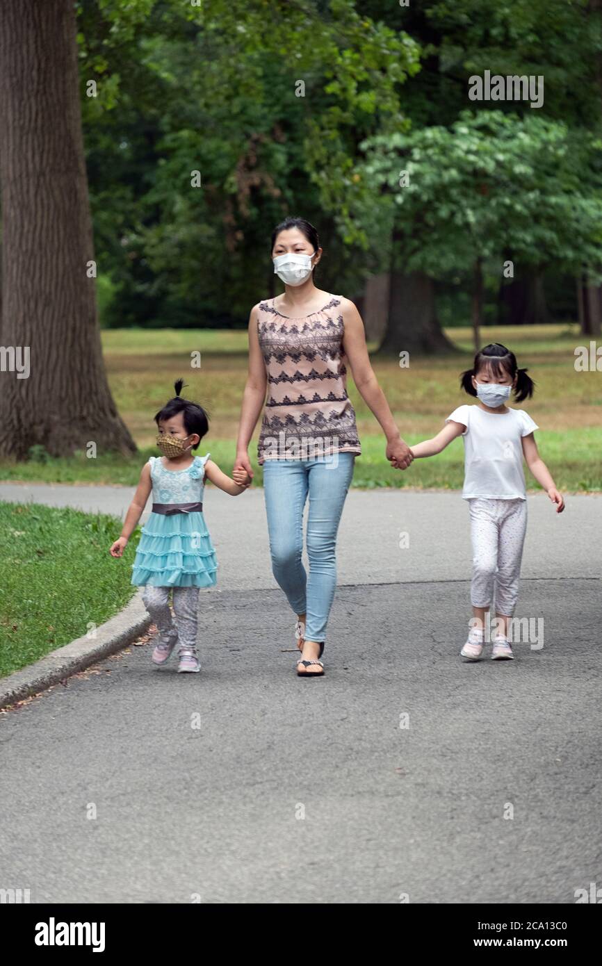 Une famille américaine asiatique, probablement chinoise, avec 2 filles très mignonnes se promener dans le parc en tenant les mains et en portant un masque chirurgical. À Queens, New York. Banque D'Images