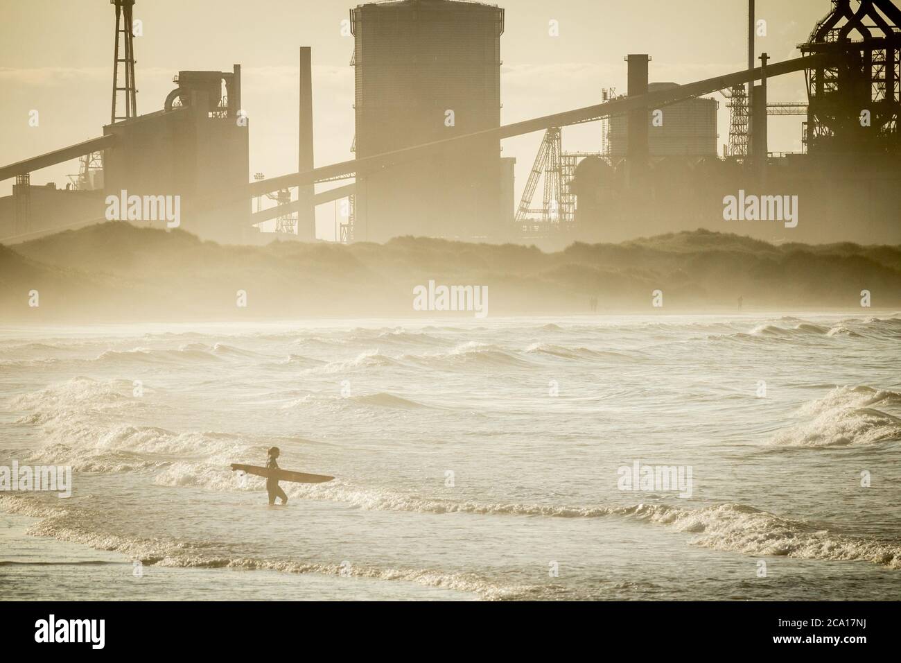 Les surfeurs se dirigeant de la plage de Redcar avec les aciéries de Redcar en arrière-plan. Banque D'Images
