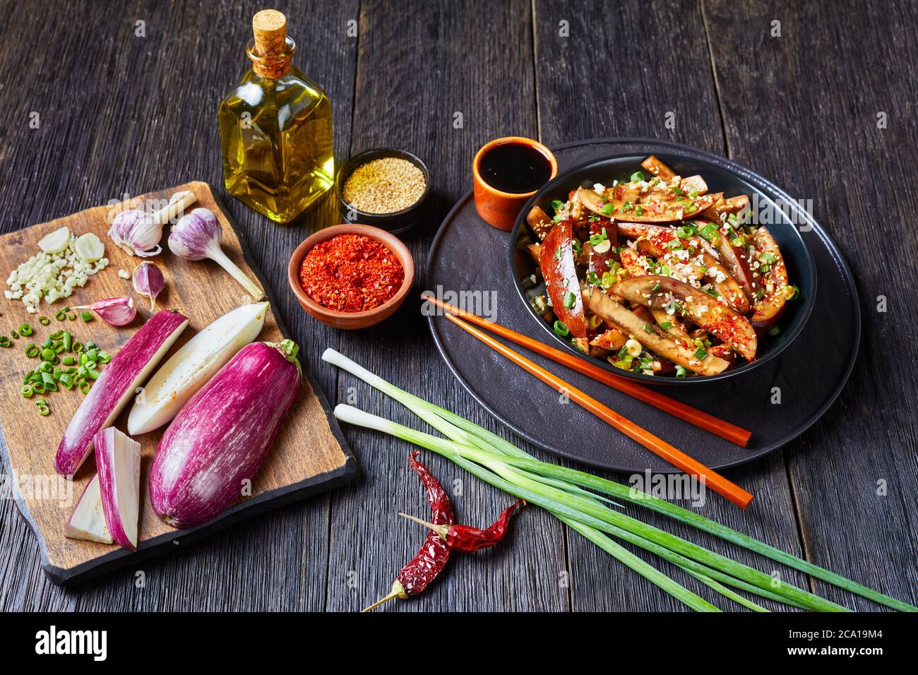 Gaji Namul, aubergine cuite à la vapeur et assaisonnée dans un bol noir sur une table en bois avec sauce soja, baguettes et ingrédients sur une planche à découper, côté coréen Banque D'Images