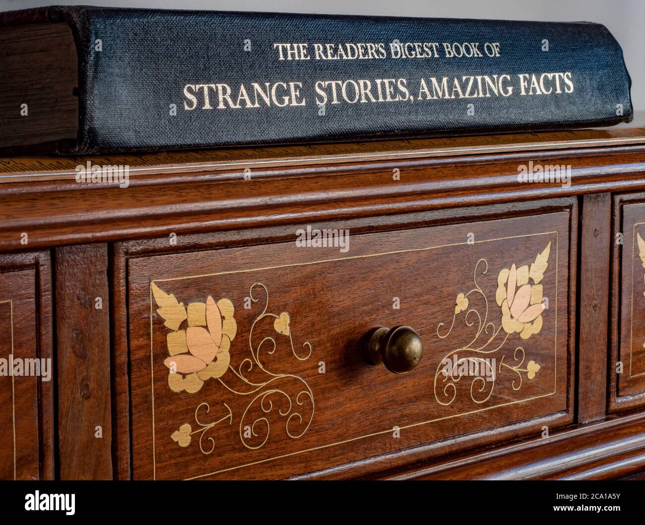 Le livre Reader’s Digest of Strange Stories, Amazing Facts (publié en 1976), en couverture rigide, sur un bureau en bois orné. Banque D'Images