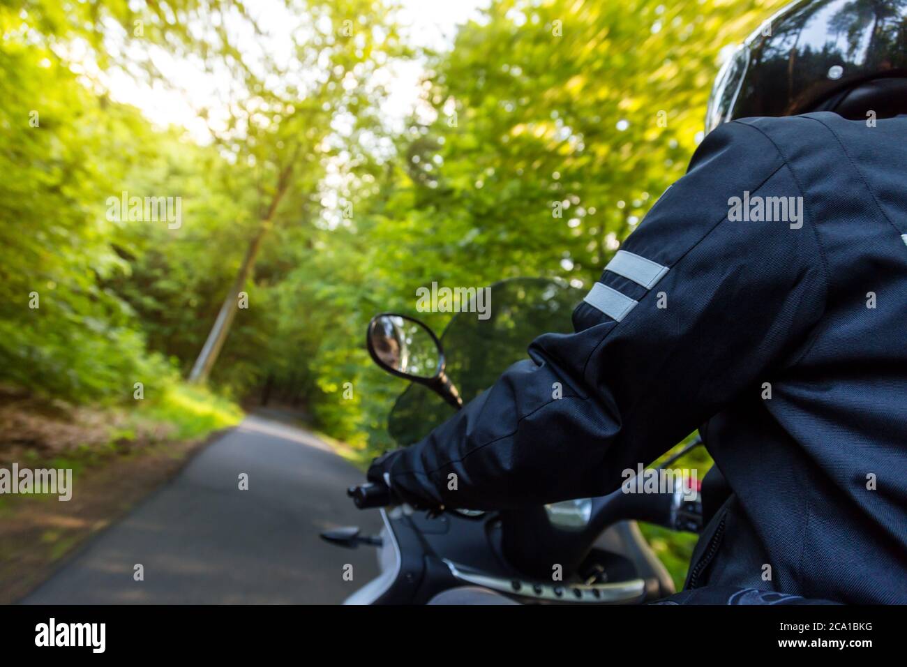 Gros plan de moto sur route vide en forêt avec lumière du coucher du soleil, concept de vitesse et de tourisme dans la nature. Banque D'Images