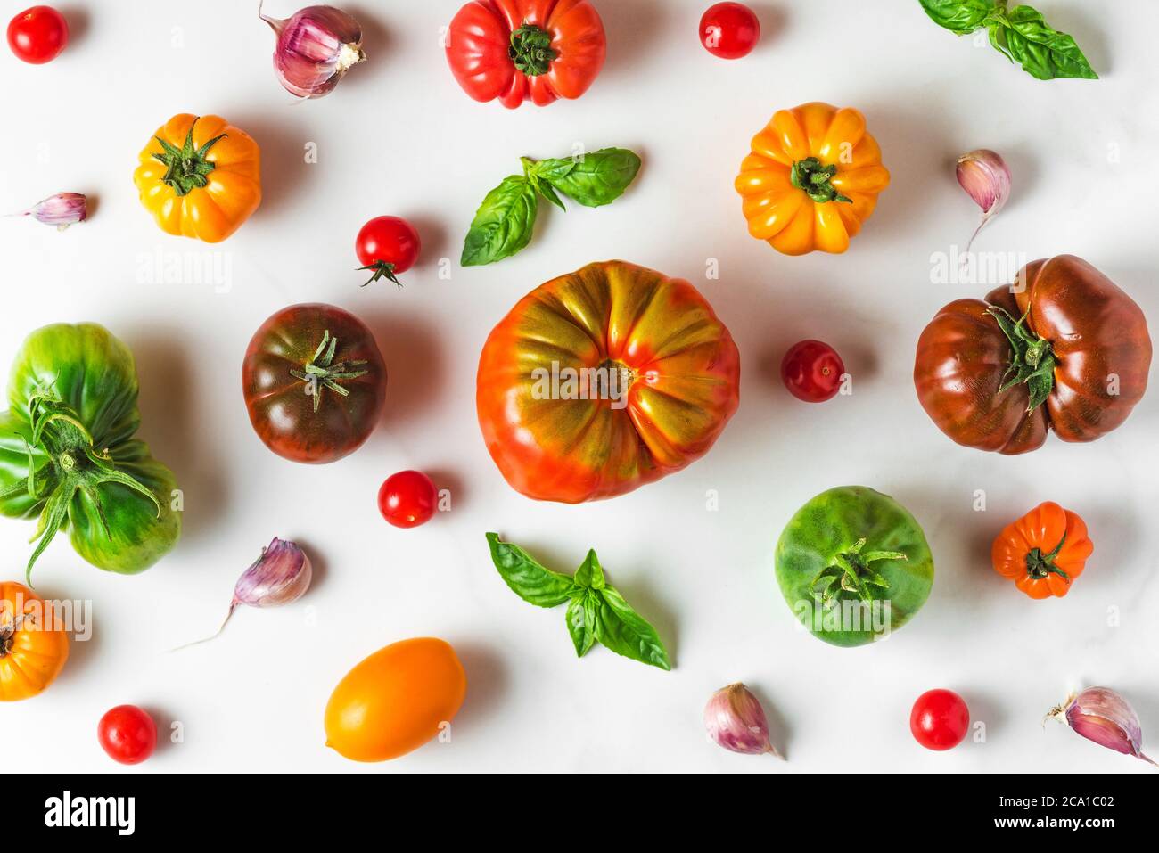composition des aliments. différentes tomates biologiques colorées, légumes au poivre, ail et basilic sur fond blanc. vue du dessus. plat Banque D'Images