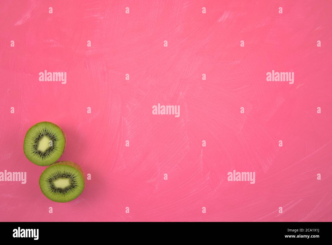 Coupé, coupé en tranches de Kiwifruits frais recouvrement isolé sur une toile de fond de grunge en acrylique rose éraillé. Espace de copie pour le texte ou l'affichage du produit. Banque D'Images