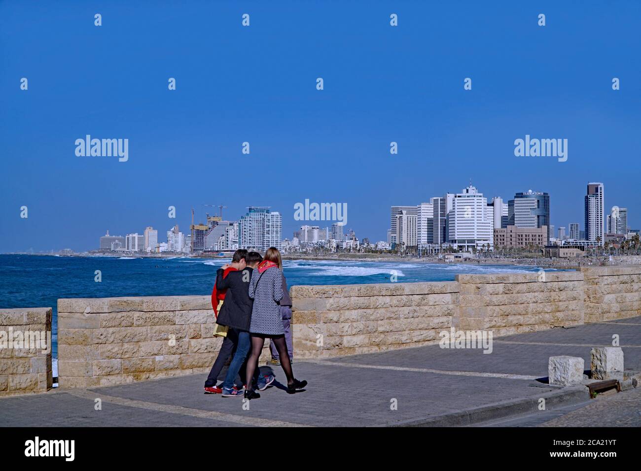 Tel Aviv, Israël - 11 janvier 2017 : trois amis marchent le long d'une promenade au bord de la mer Méditerranée, avec la ville en toile de fond. Banque D'Images