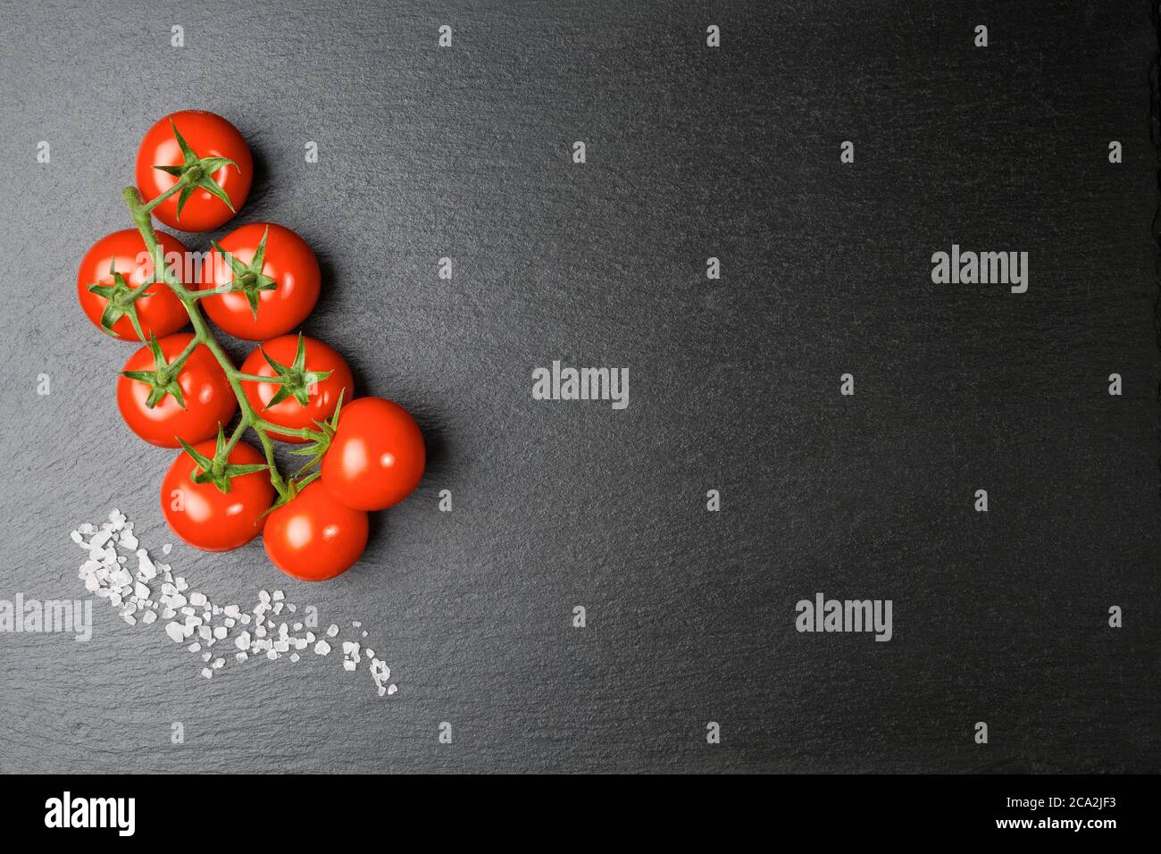 Une branche de tomates cerises avec quelques grains de sel épais sur une dalle d'ardoise Banque D'Images