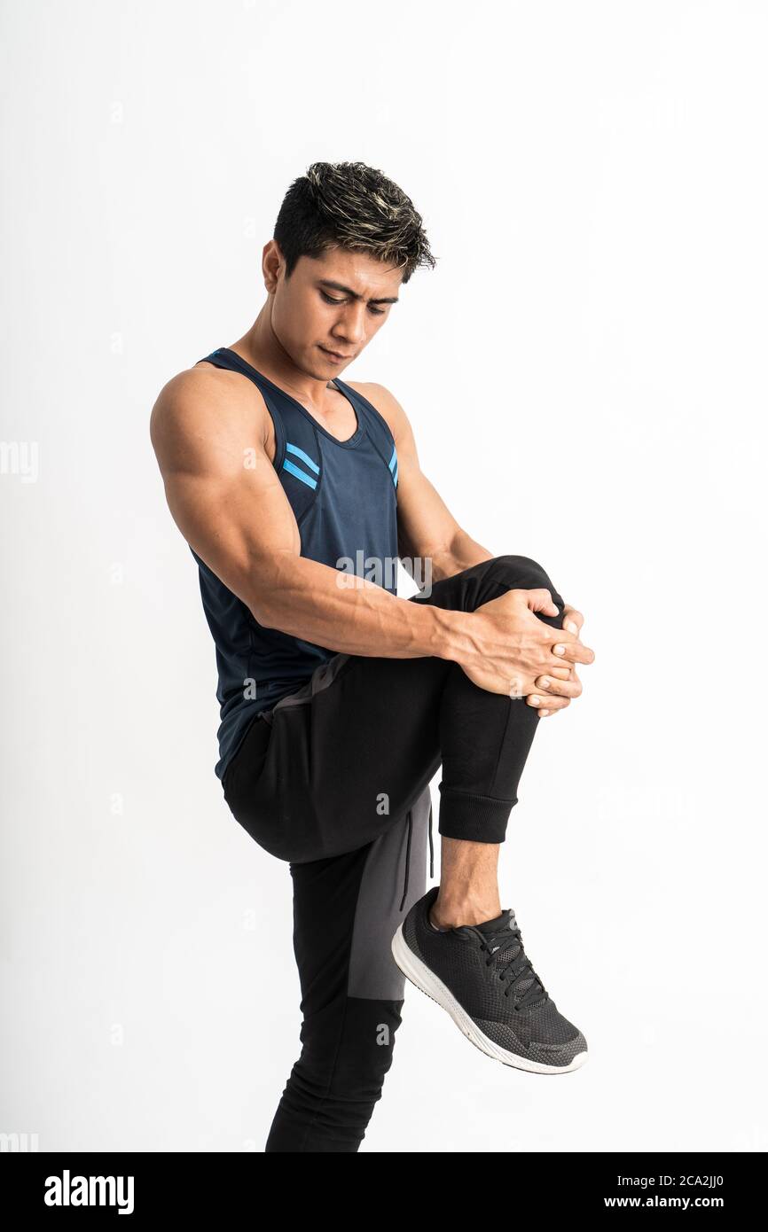 muscle homme portant des vêtements de sport se tient face à côté de la jambe s'étire en soulevant la jambe devant l'estomac sur un arrière-plan isolé Banque D'Images