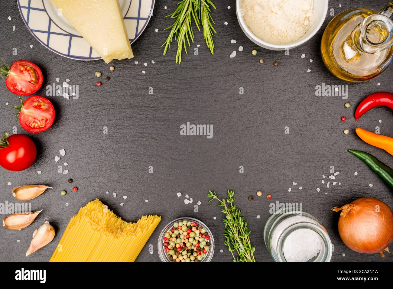 Spaghetti Napoli ingrédients sur une plaque d'ardoise.avec thym, romarin, oignon, poivrons chauds, grains de sel grossiers, grains de poivre coloré, gousses d'ail, parmesan. Banque D'Images