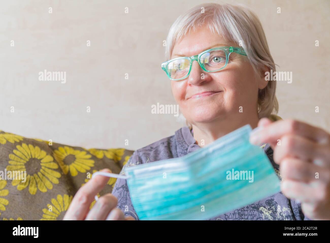 Femme âgée souriante prenant un masque de protection à la maison. Femme âgée avec masque de visage entre les mains. Une femme souriante prend son masque médical après le retour Banque D'Images
