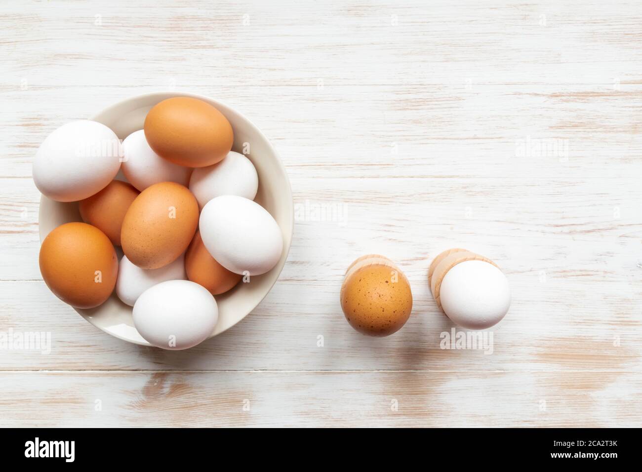 Faire un bol avec des œufs de poulet brun et blanc et des œufs durs dans les supports sur la table. Œufs dans une assiette et supports sur fond de bois. Œufs biologiques gratuits. Banque D'Images