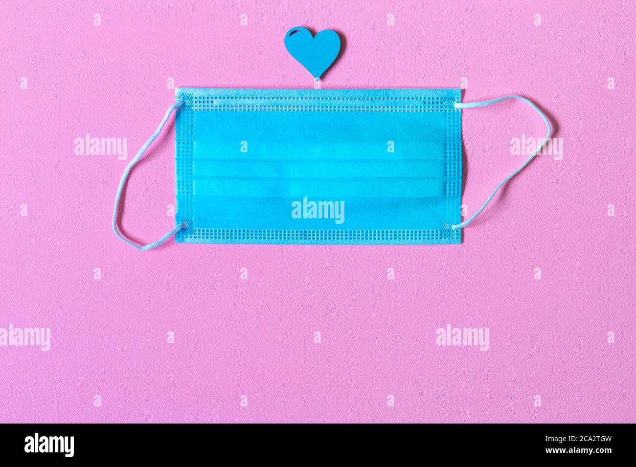 Masque médical jetable bleu et symbole de coeur sur fond rose. Masque turquoise et coeur sur tableau rose. Merci au personnel médical. Appreci Banque D'Images