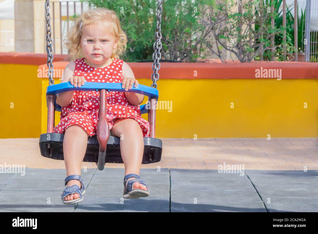 Petite fille blonde sur balançoires à l'extérieur dans l'aire de jeux. Balancement pour tout-petits. Jolie fille en rouge à pois balançoires dans l'aire de jeux publique. Petite fille s'amuser Banque D'Images