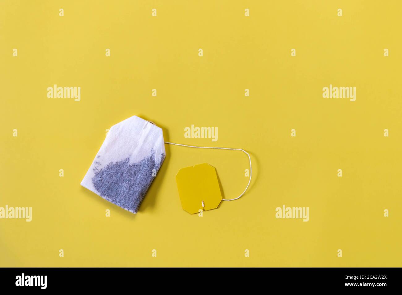 Sachet de thé avec étiquette sur fond jaune plat. Sachet de thé vert carré sur fond jaune avec espace de copie. Teabag et étiquette jaune. Bannière large avec Banque D'Images