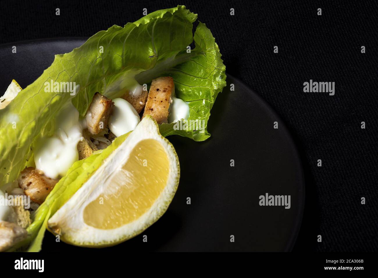 Salade César maison avec poulet, laitue, citron, toasts, sauce césar, fromage et ail. Sur fond sombre. Concept d'alimentation saine. Banque D'Images