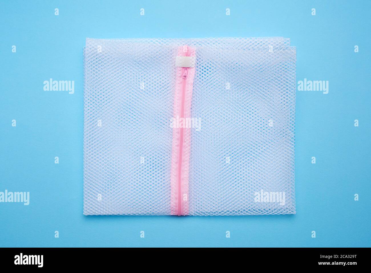 sac pour laver les vêtements dans le tambour d'un lave-linge à partir d'un filet blanc, fond bleu. Banque D'Images