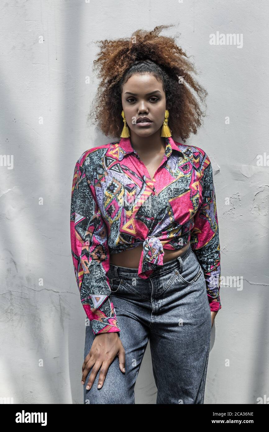 Jeune modèle afro-américain élégant avec coiffures afro-américaines et  boucles d'oreilles à pampilles brillantes portant une chemise colorée  tendance avec noeud et Jean Photo Stock - Alamy