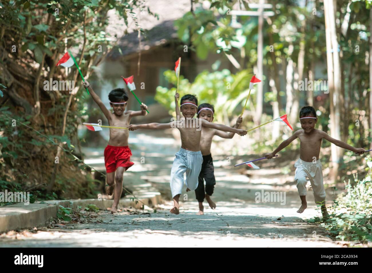 avoir un groupe amusant d'enfants courir sans vêtements pourchassant chacun autre lorsque vous tenez le petit drapeau rouge et blanc et a soulevé le drapeau sur un fond d'arbre Banque D'Images