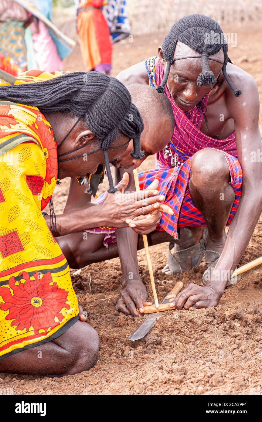 Trois tribesmen de maasai, portant une tenue traditionnelle, faisant feu avec deux bâtons dans un village de maasai. Réserve nationale de Maasai Mara. Kenya. Afrique. Banque D'Images