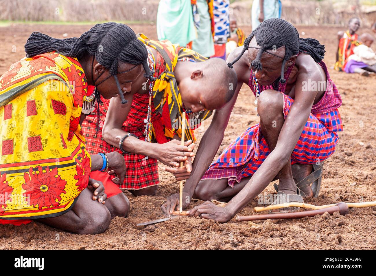 Trois tribesmen de maasai, portant une tenue traditionnelle, faisant feu avec deux bâtons dans un village de maasai. Réserve nationale de Maasai Mara. Kenya. Afrique. Banque D'Images