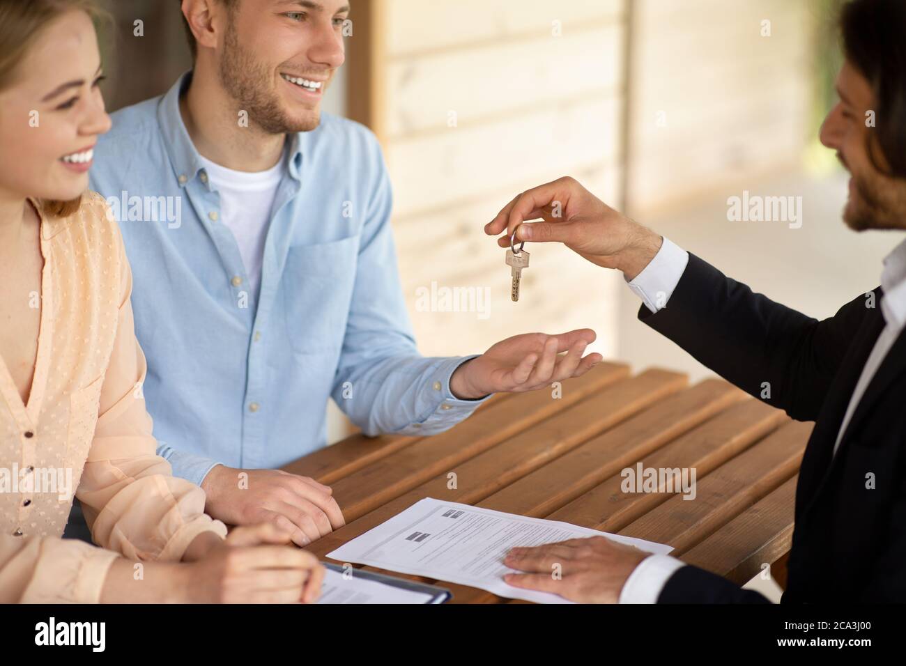 Un agent immobilier qui donne les clés de la nouvelle maison à un couple heureux et marié à la table à l'extérieur Banque D'Images Un agent immobilier qui donne les clés de la nouvelle maison à un couple heureux et marié à la table à l'extérieur Banque D'Images