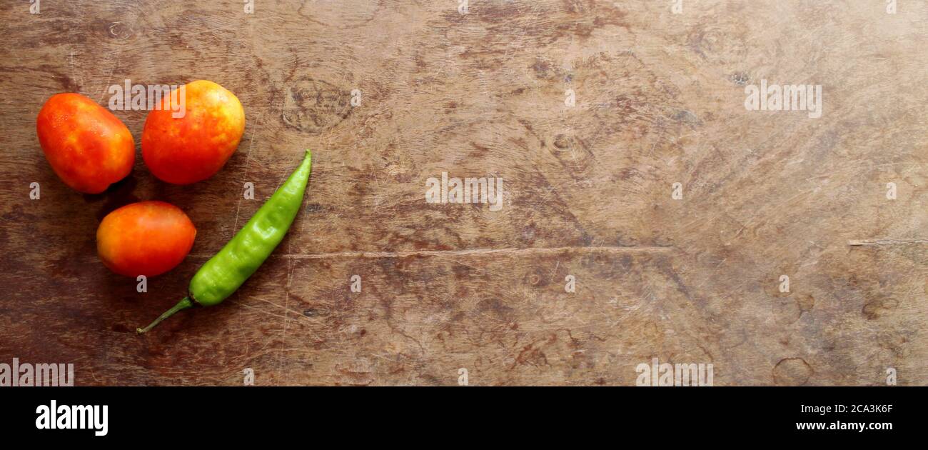 Tomates et piment vert sur une table en bois. Espace vide pour le nom de marque/la ligne de pointage. Banque D'Images