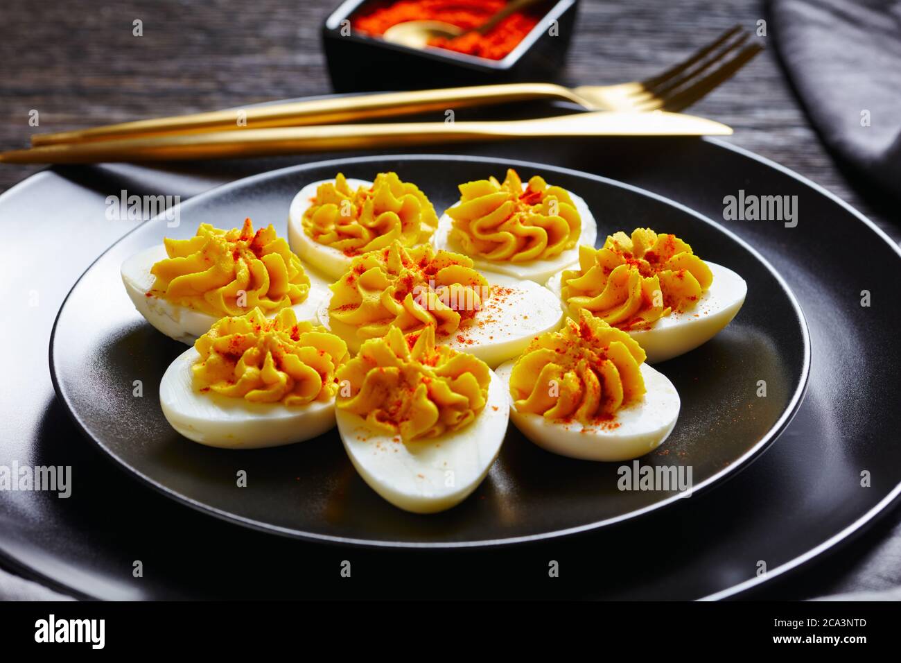 Simple œufs défaits de moutarde aux jaunes d'œufs, mayonnaise, vinaigre blanc arrosé de paprika fumé sur une assiette noire sur fond de bois sombre Banque D'Images