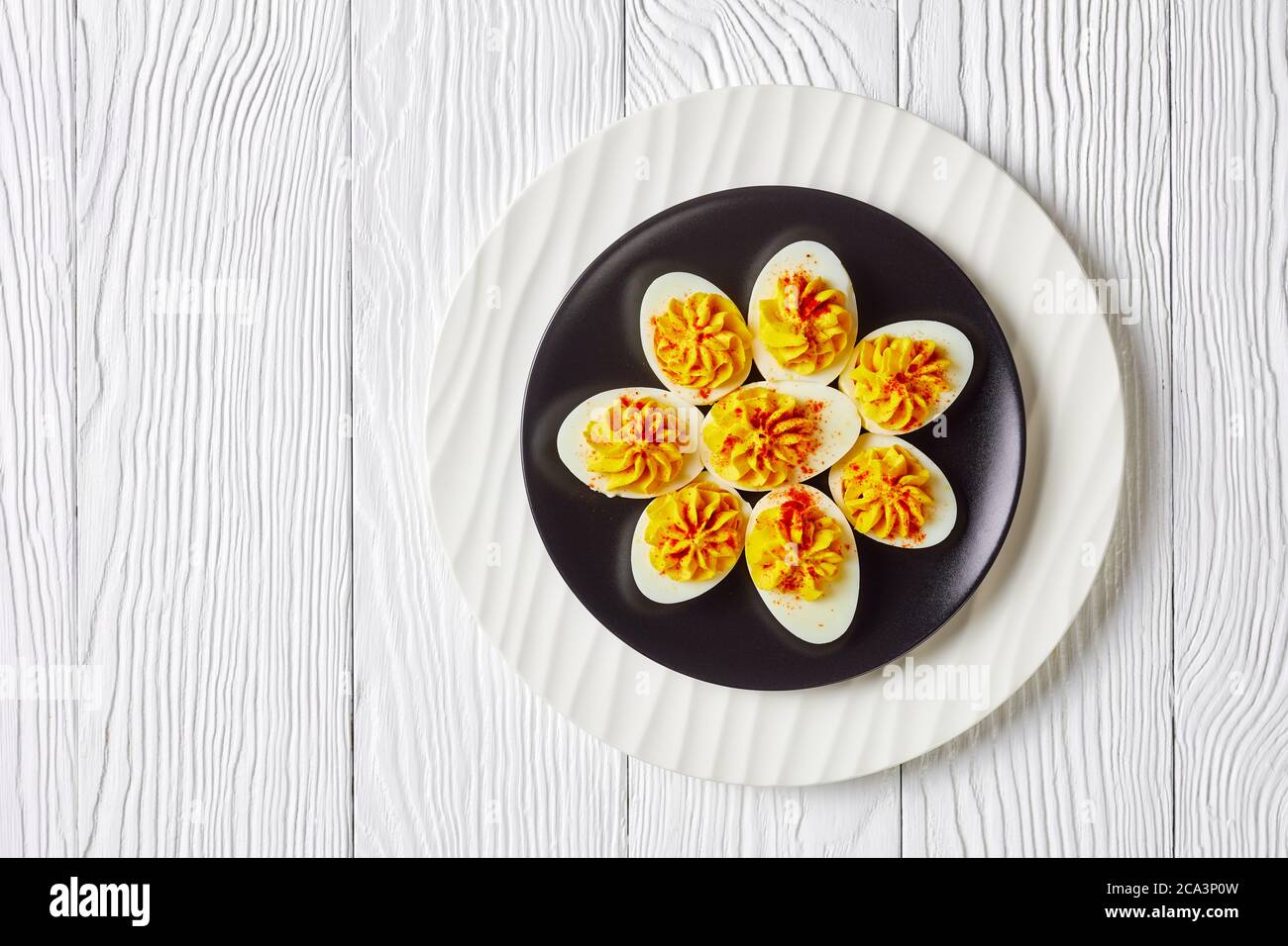 Œufs américains dévorés de jaunes d'œufs, moutarde de dijon, mayonnaise, vinaigre de cidre de pomme parsemé de paprika fumé sur une assiette noire sur un W blanc Banque D'Images