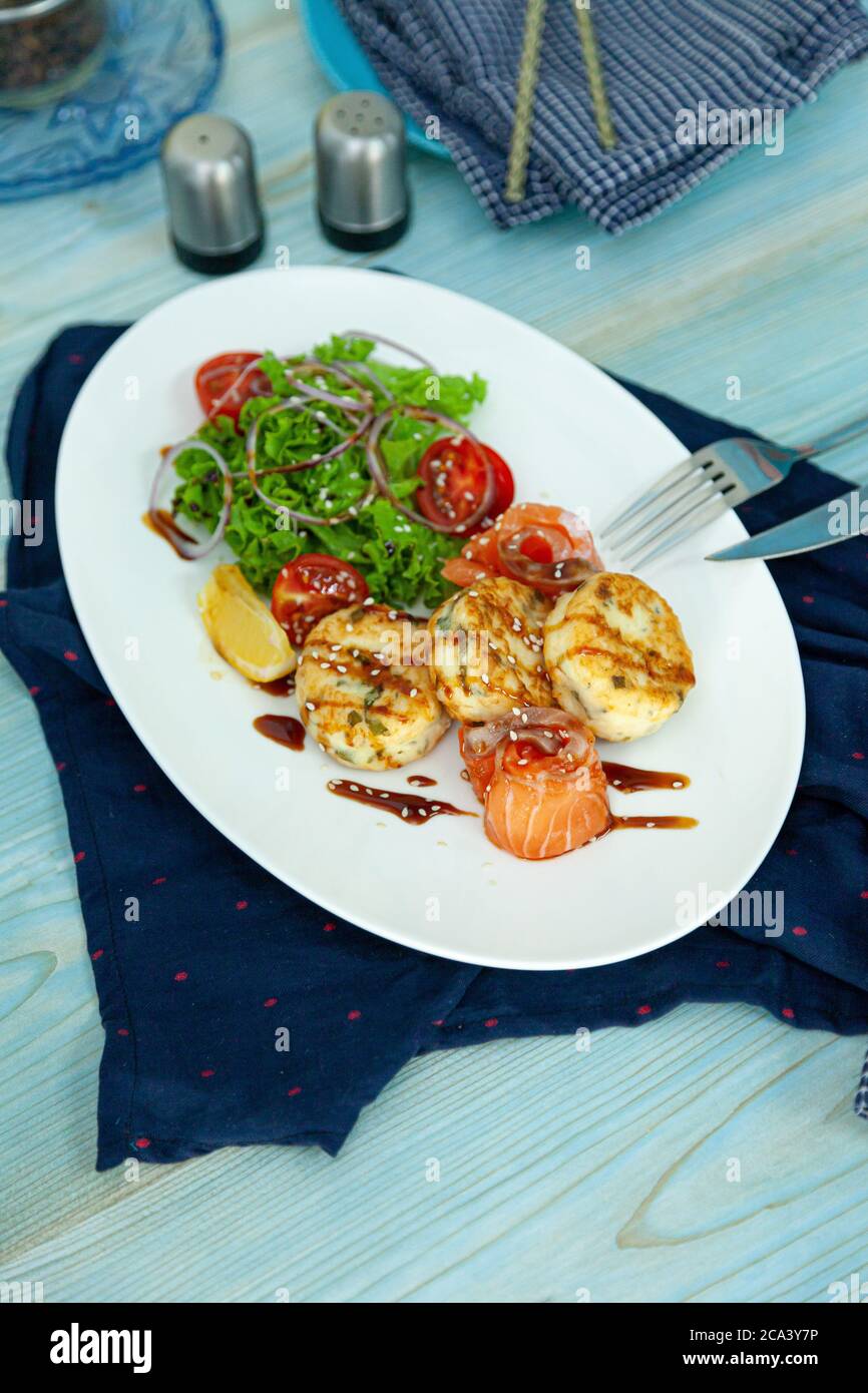 Des gâteaux de poisson avec salade, tomates et oignons rouges dans un restaurant sur une assiette blanche. Saumon rouge. Menu poisson. Gros plan. Nourriture saine Omega-3 sur bleu Banque D'Images