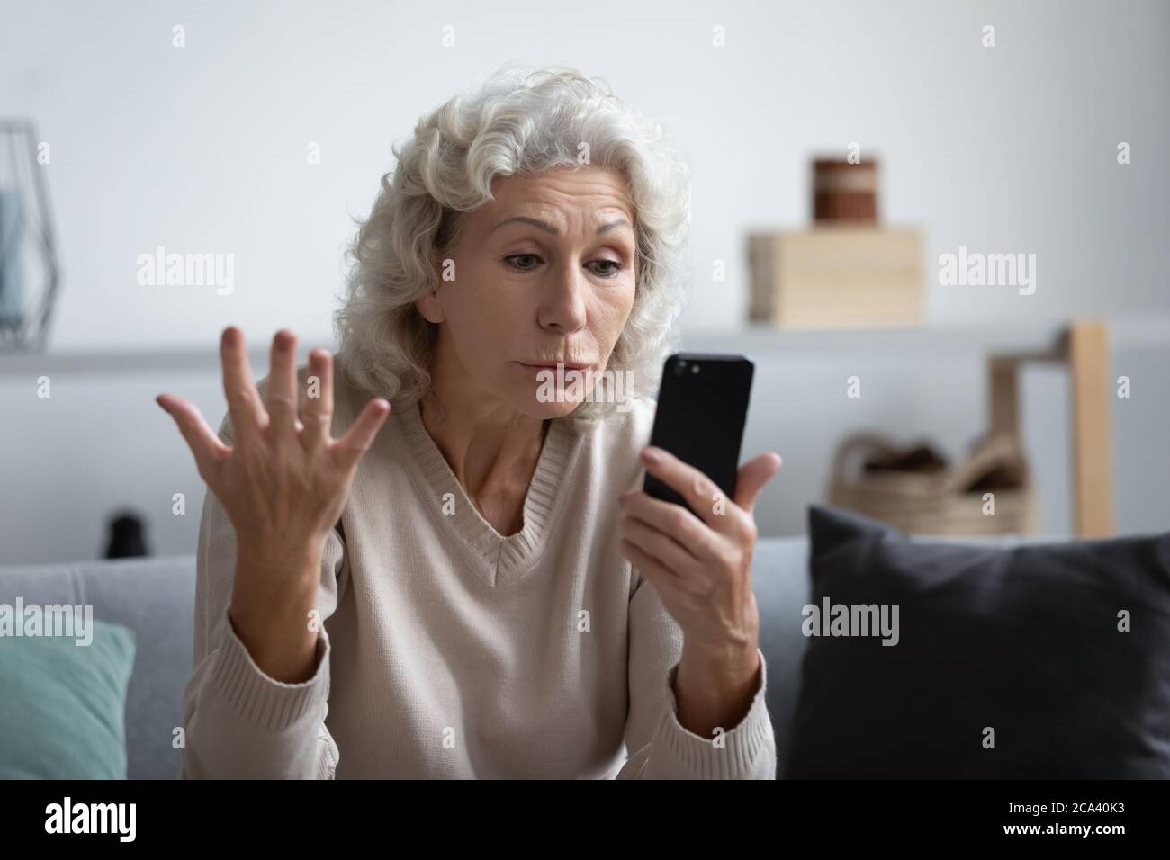 La grand-mère qui tient le smartphone regarde l'écran de l'appareil semble en colère Banque D'Images