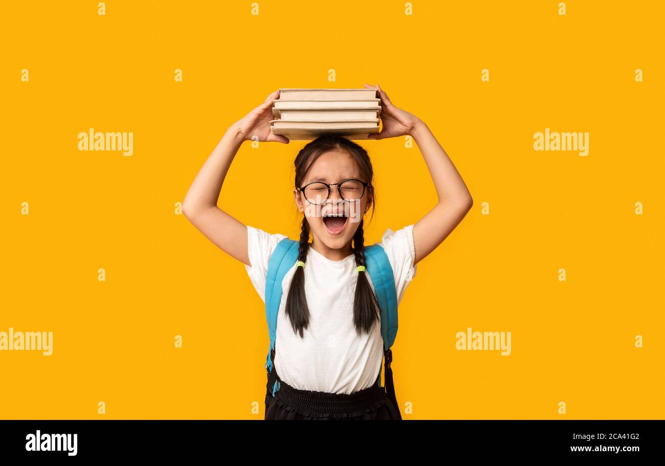 Discontent Japanese Girl Shcriting tenant des livres sur la tête, fond jaune Banque D'Images