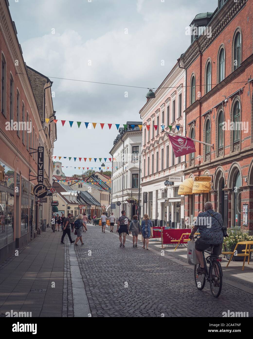 Lund, Suède - 4 août 2020 : une petite rue pavée dans la ville universitaire avec des bannières colorées pendues au-dessus de lui pendant que les gens marchent et Banque D'Images