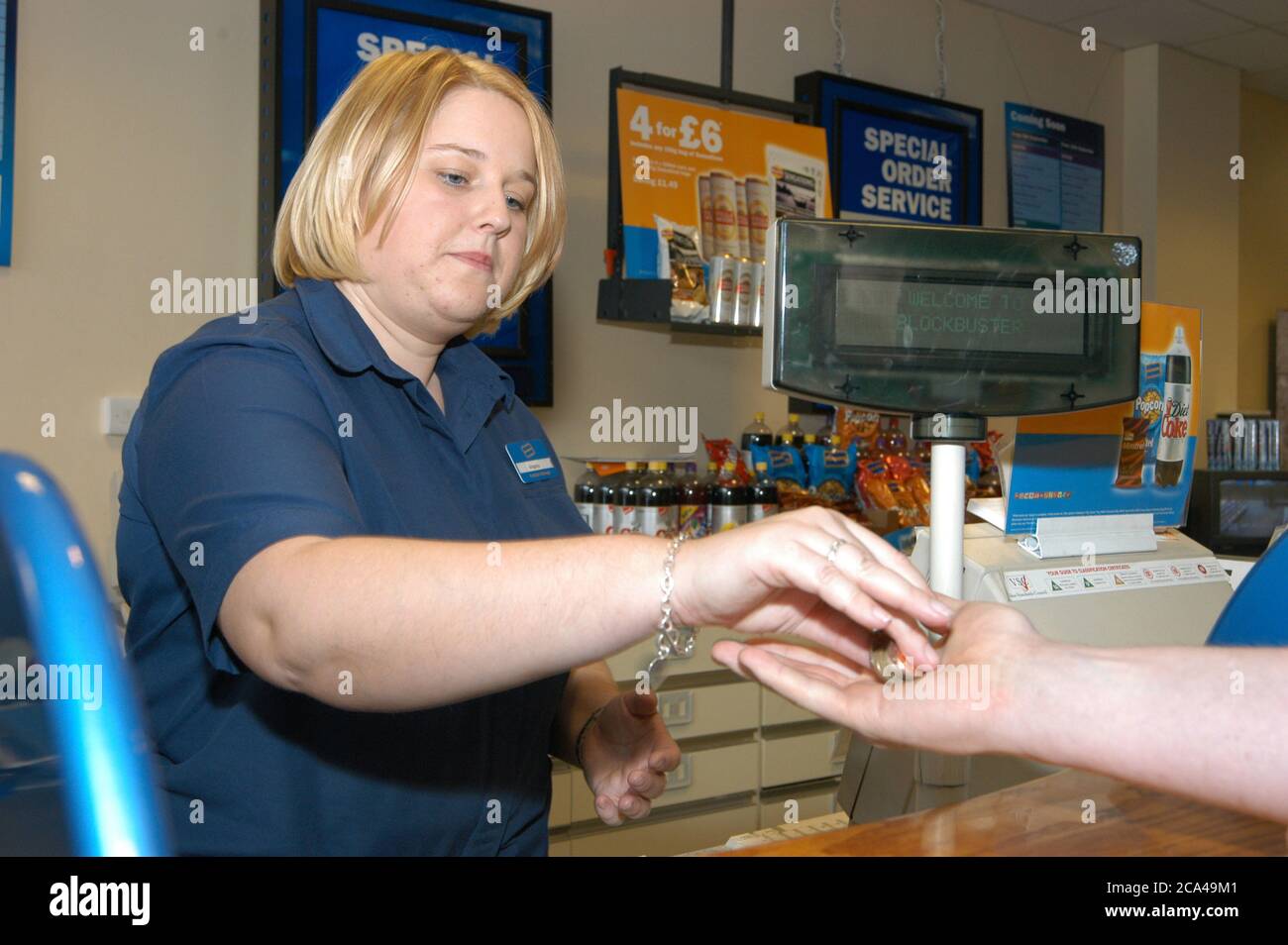 Jeune femme travaillant dans la boutique de location de vidéos Blockbuster au service d'un client; Merseyside Banque D'Images