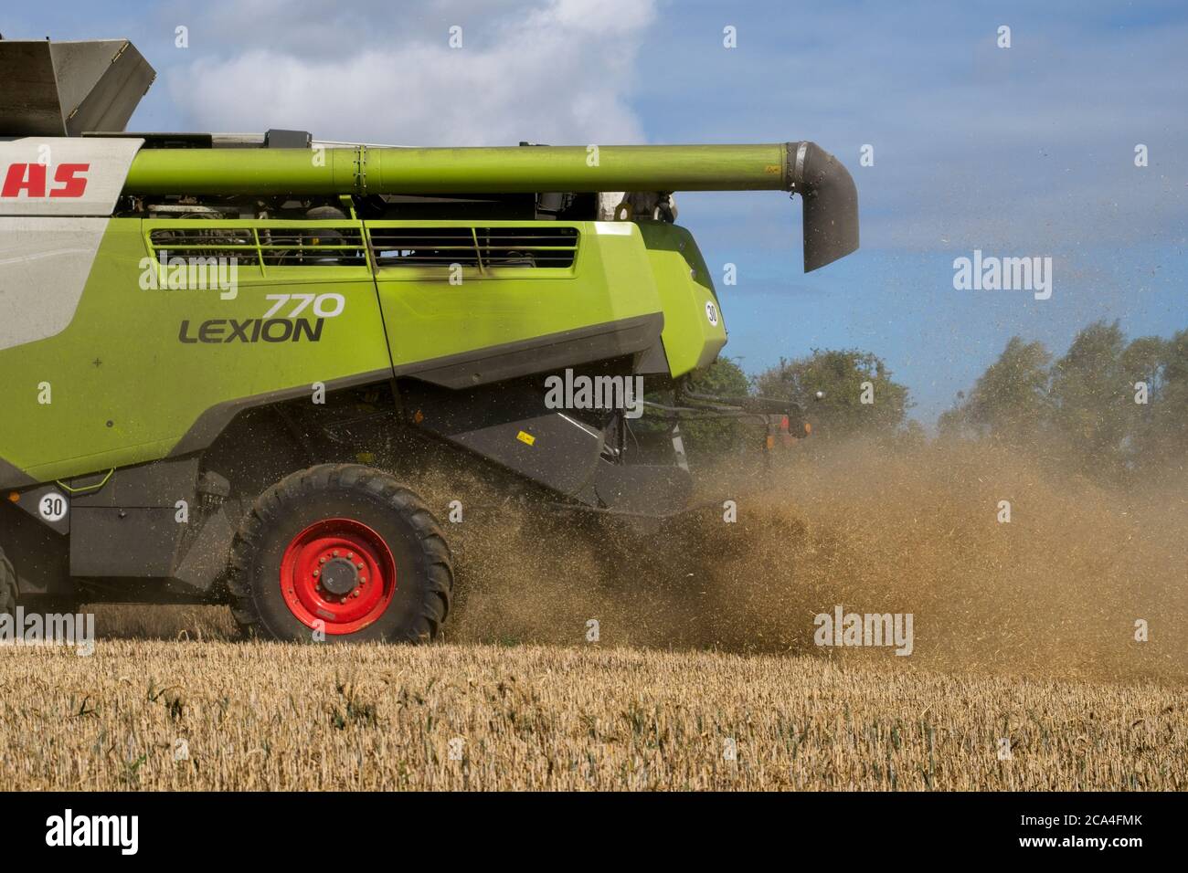 Récolte d'hiver vue rapprochée de l'arrière de la moissonneuse-batteuse combinée à Travail sur le terrain poussiéreux ensoleillé ciel nuageux champs arbres et Maisons au format distance Paysage Banque D'Images