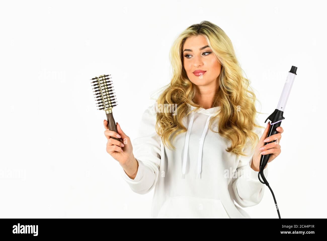 Conseils de coiffeur. Créez une coiffure avec un fer à friser. Une femme  aux cheveux longs et bouclés utilise un fer à friser. Adorable fille  blonde. Acheter des outils. Boutique en ligne.