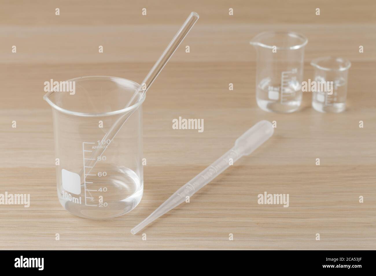 bécher en verre de mesure transparent de 100 ml avec tige en verre et  pipette en plastique et deux béchers plus petits à l'arrière sur table en  bois, idée de prendre des