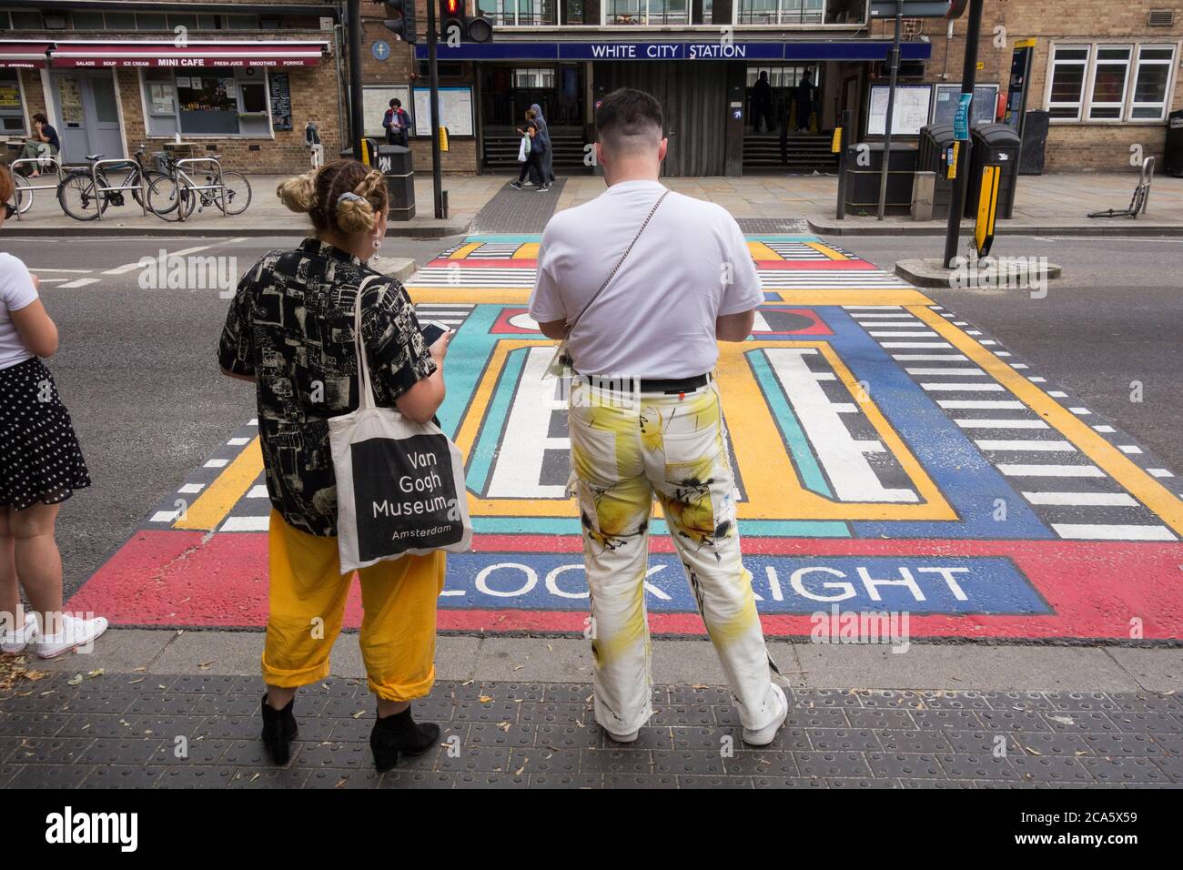 Un couple attend à côté des passages géométriques pour piétons de l'artiste français Camille Walala devant la station de métro White City à l'ouest de Londres, Royaume-Uni Banque D'Images