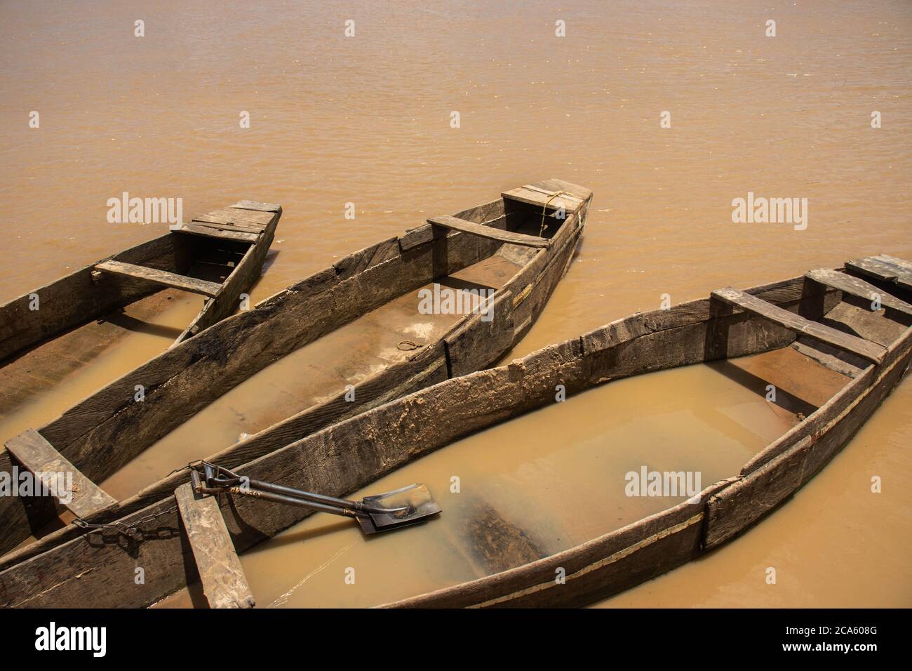 Trois vieux bateaux en bois amarrés sur une rivière sale. Un des bateaux a deux pelles en elle. Banque D'Images