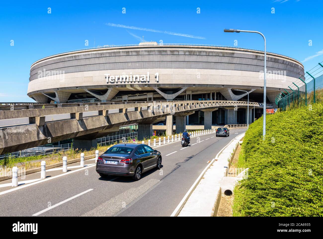 Les voitures de tourisme atteignent le bâtiment circulaire du terminal 1 de l'aéroport Paris-Charles de Gaulle par la route d'accès par une journée ensoleillée. Banque D'Images