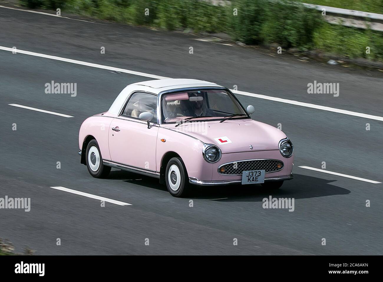 Une voiture Nissan Figaro Pink car Cabriolet essence 2011 conduite sur l'autoroute M6 près de Preston dans Lancashire, Royaume-Uni Banque D'Images