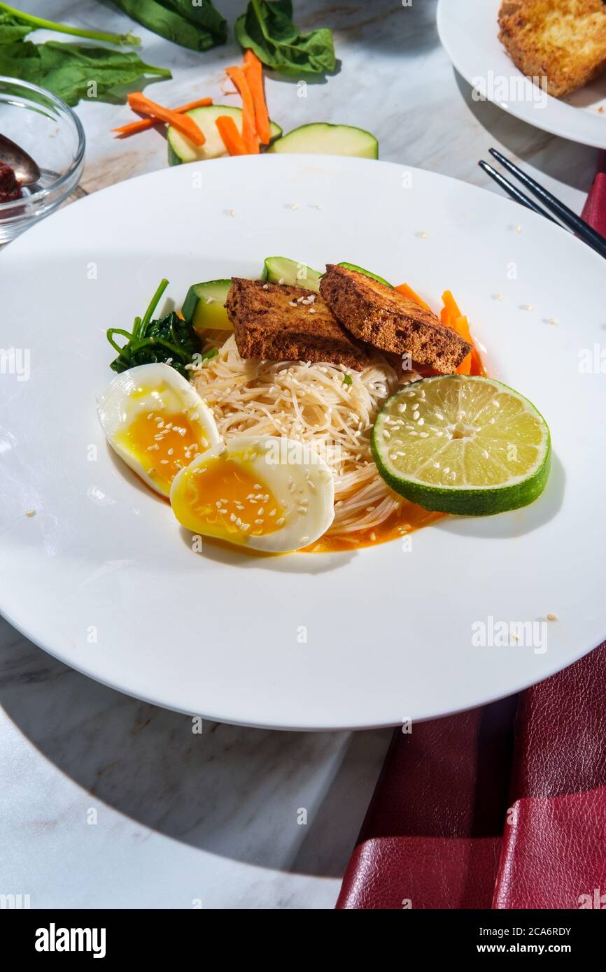 Soupe thaïlandaise de nouilles de riz au curry rouge accompagnée de tofu frits croustillants et d'œufs durs Banque D'Images