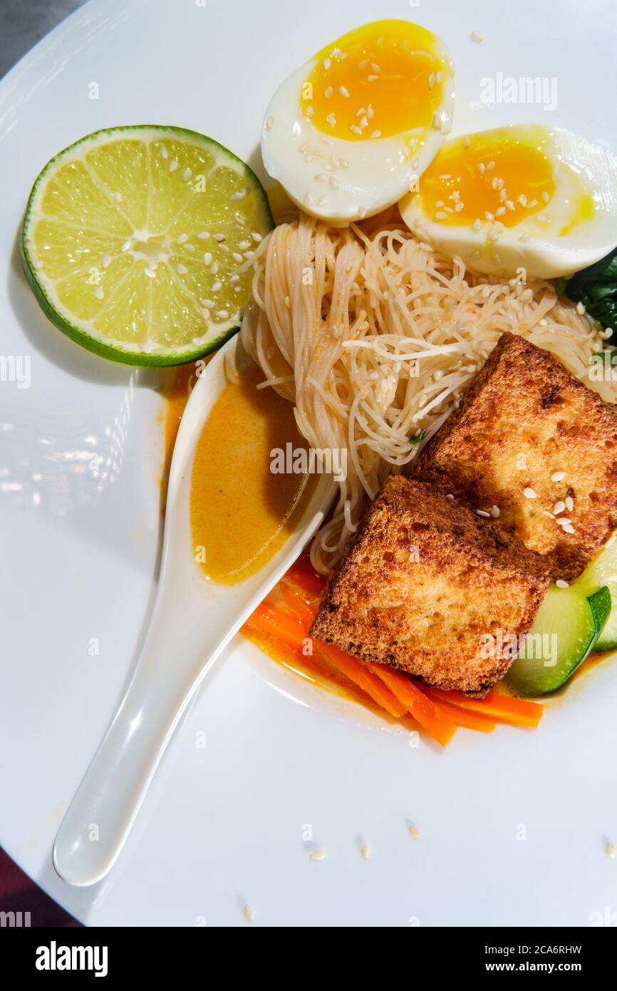 Soupe thaïlandaise de nouilles de riz au curry rouge accompagnée de tofu frits croustillants et d'œufs durs Banque D'Images