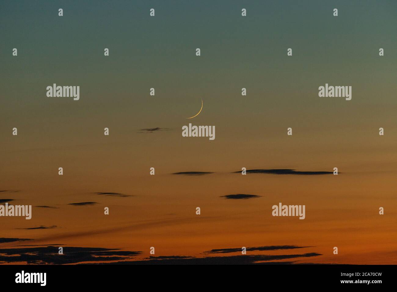 Lune en croissant qui brille dans un ciel orange au coucher du soleil. Banque D'Images