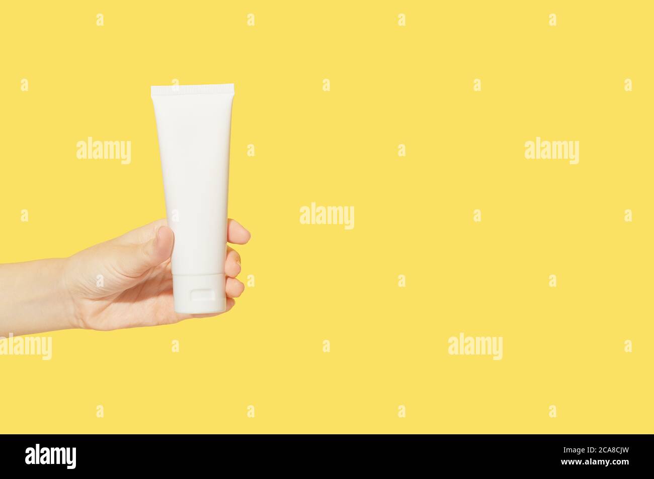 Crème pour les mains et les ongles dans un contenant en plastique blanc dans une main femelle sur un isolat de fond jaune. Lotion pour le soin du corps. Simple emballage vide beauté cosm Banque D'Images