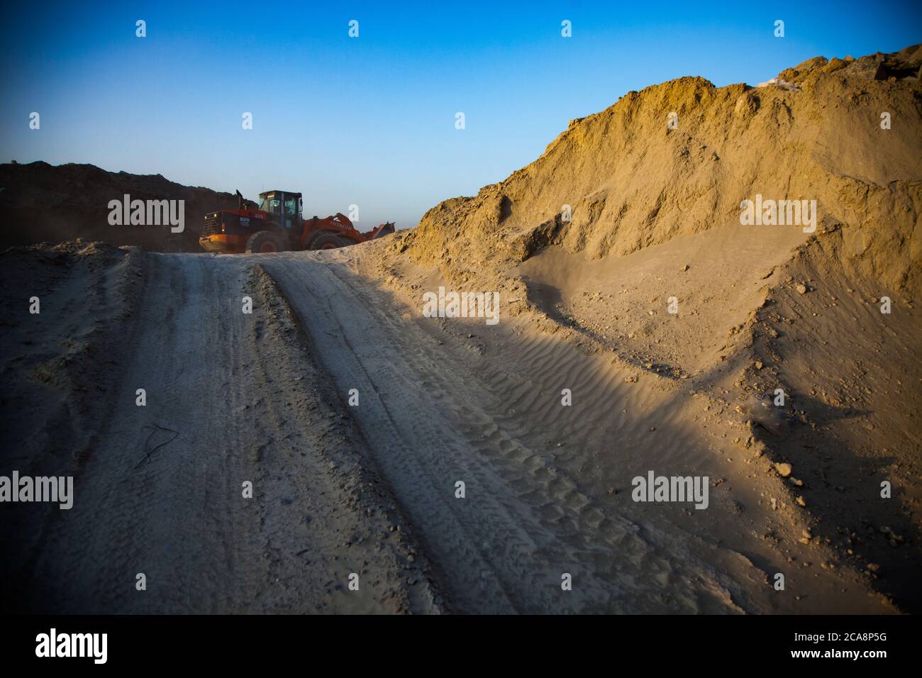 Carrière d'une usine d'extraction et de traitement de l'or. Tas de sable ou de terre et tracteur Orange (bulldozer) fonctionne. Banque D'Images