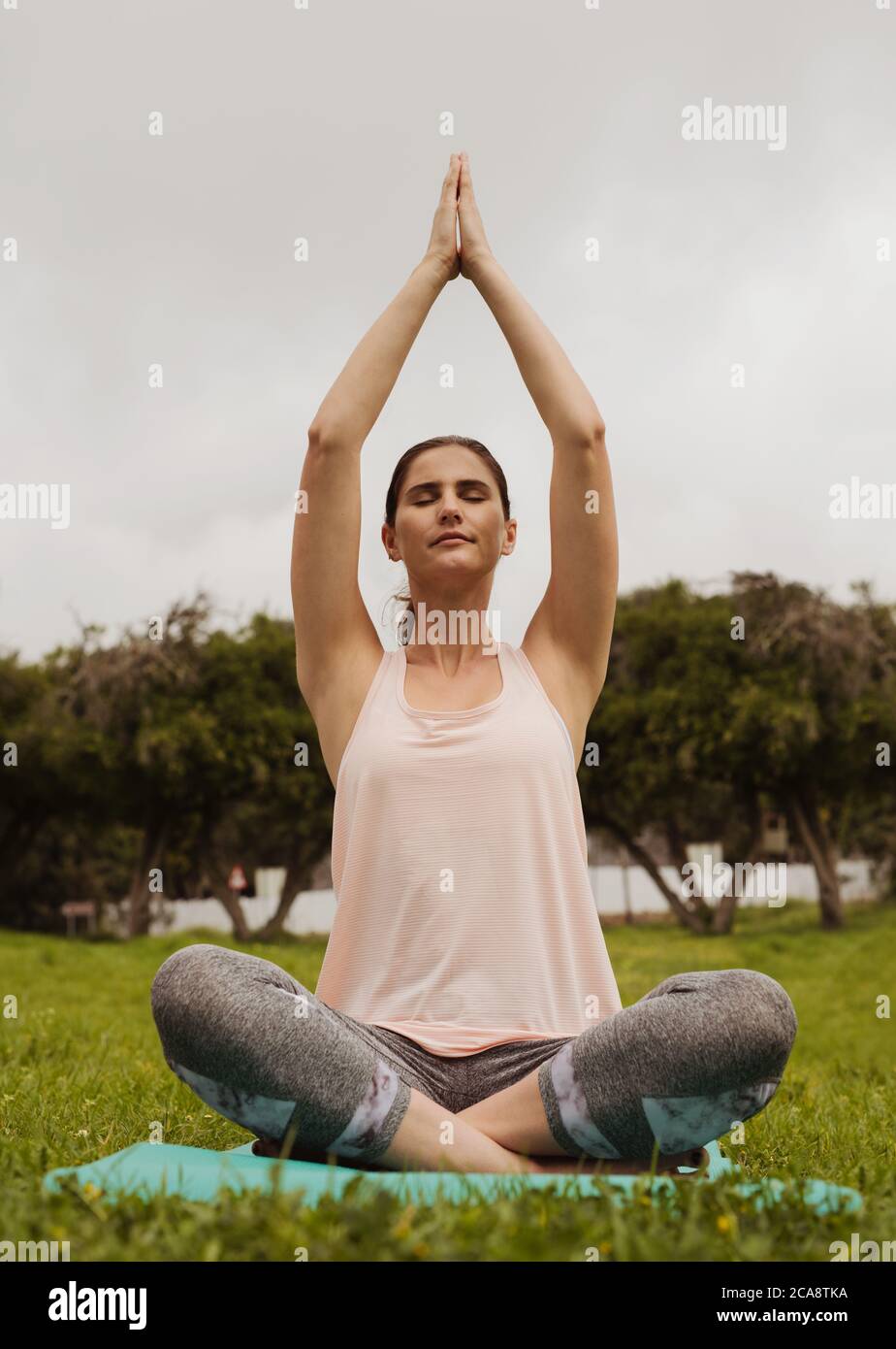 Gros plan d'une femme de fitness assise dans une posture de yoga dans un parc. Femme pratiquant le yoga assise dans un parc avec des paumes jointes au-dessus de sa tête. Banque D'Images