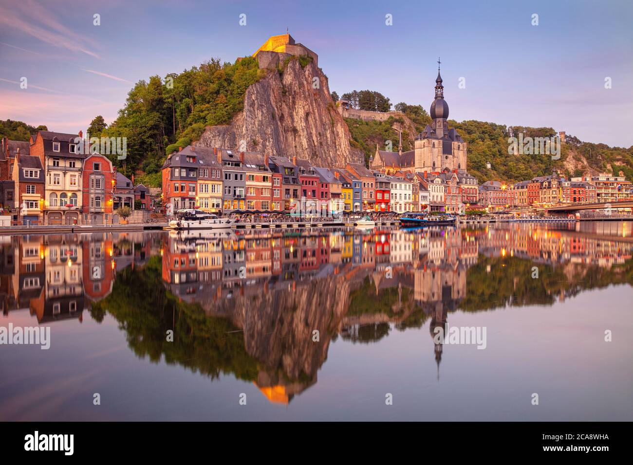 Dinant, Belgique. Image de paysage urbain de la belle ville historique de Dinant avec le reflet de la ville dans la Meuse au coucher du soleil d'été. Banque D'Images